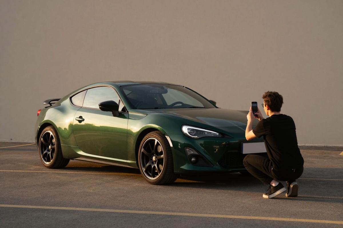 Photographer capturing a front three-quarter photo of a sports car with a smartphone during golden hour