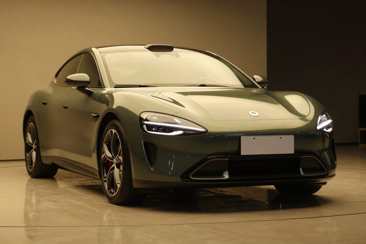 Dark green sports car under warm showroom lighting on a reflective studio floor, staged for a cinematic car reel style shot