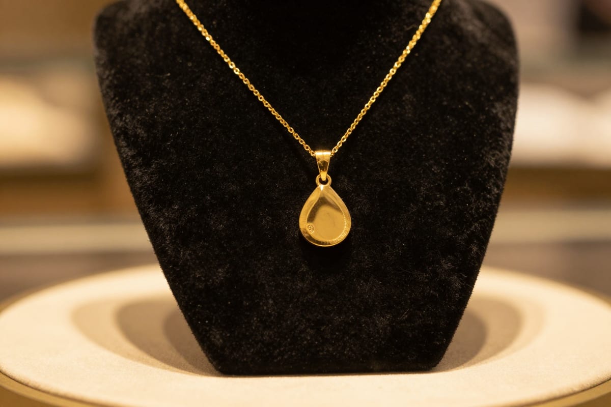 Gold pendant necklace rotating under warm jewelry-counter lighting, the orbit and macro style for a jewelry reel from photos
