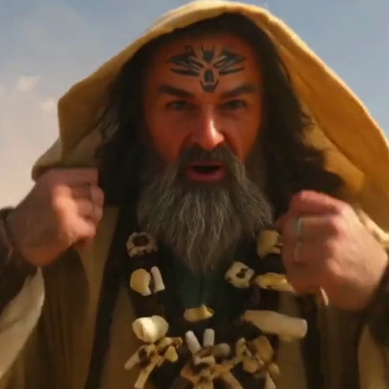 Close crop of a frame from one of our AI-generated clips, original file: a bearded man in a hood with a forehead mark, sharp beard strands and clear knuckles