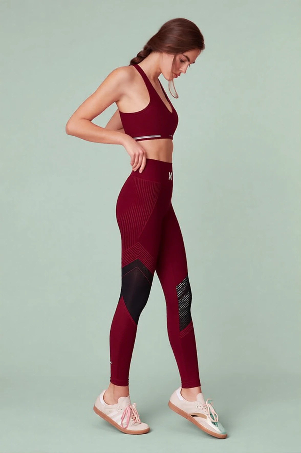 The same frame recolored to a deep burgundy set with ribbed knit across the hip and a black mesh panel down the lower leg, on a soft sage green backdrop