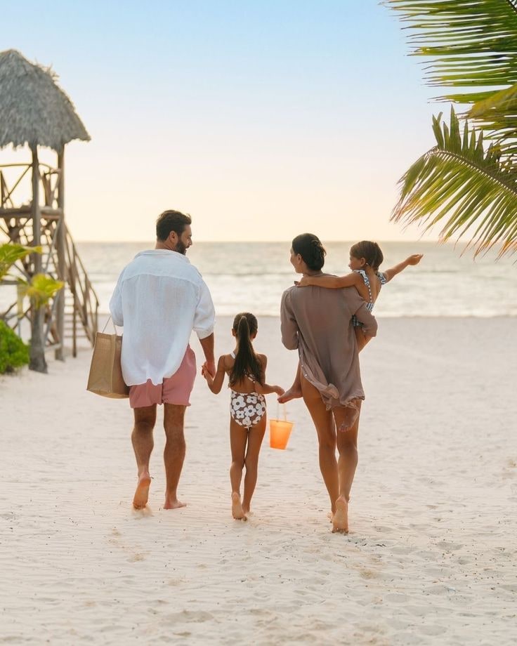 The source photo: a family of four walking away down a sunlit beach — father in a white shirt carrying a tote, a girl with an orange bucket, mother carrying a toddler, a thatched lifeguard tower on the left