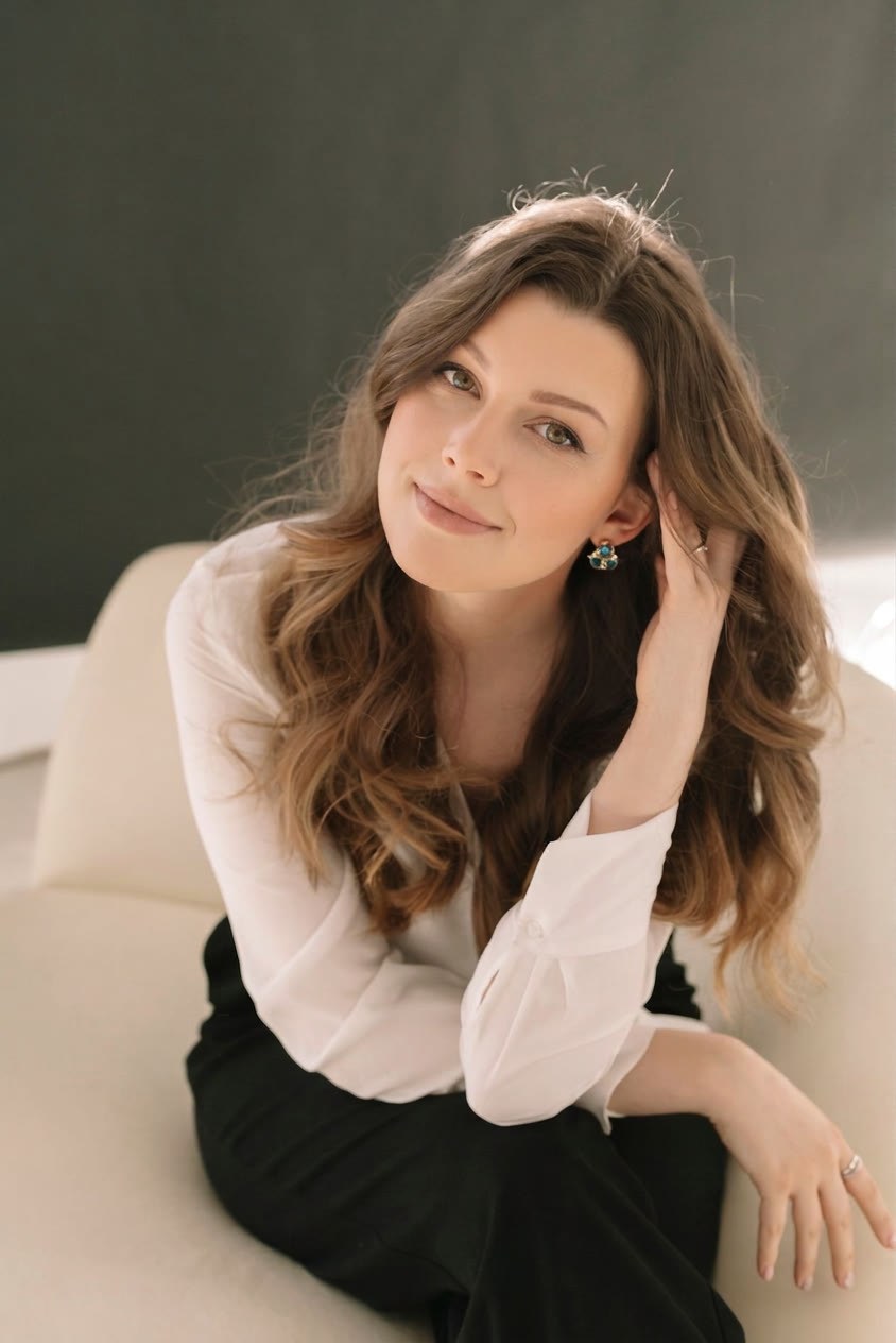 The same frame after the fix: her eyes are open and looking at the camera with a soft, natural smile, while her face, hair, hand, clothes and the room behind her are untouched