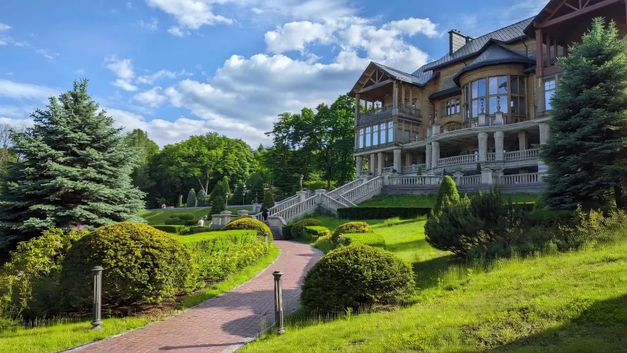 A frame from the video generated from that photograph — the camera has drifted back and left, opening up the lawn and the sky while the lodge keeps its detail