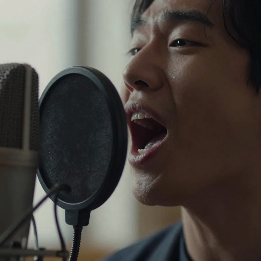 Extreme close-up of a singer's open mouth mid-note beside a pop filter and the grille of a large-diaphragm microphone