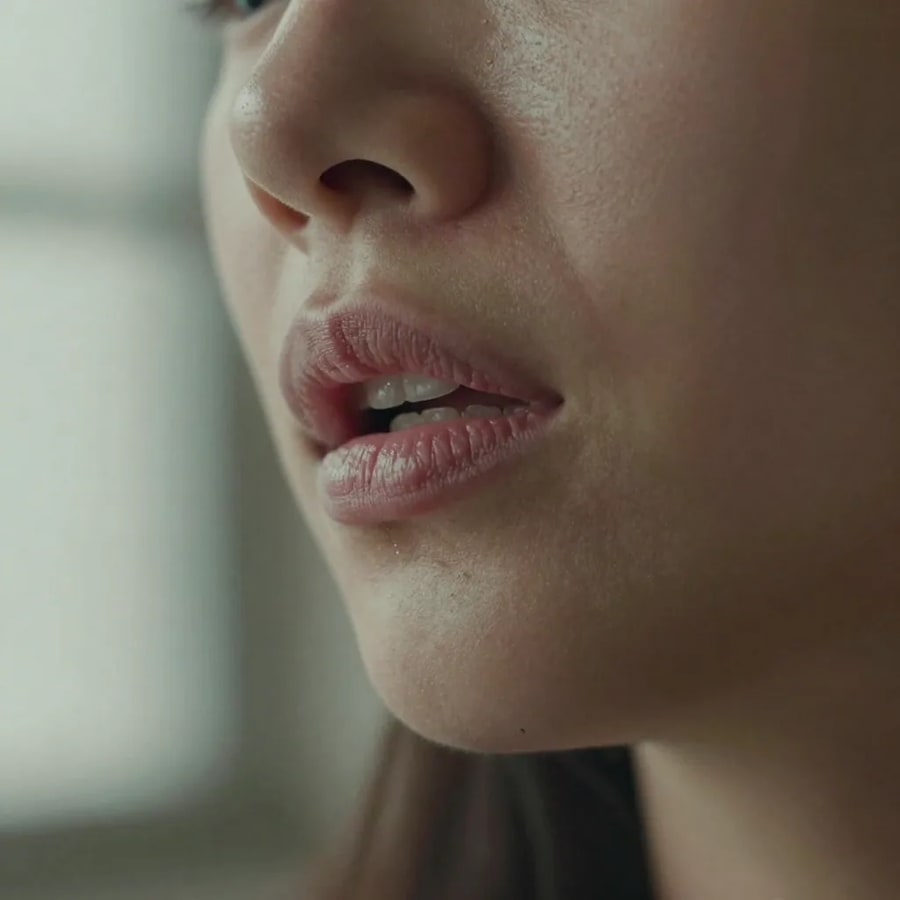 Close-up of a woman’s mouth and jaw forming a word in soft side light, shallow focus — the rhythm and emphasis of real speech that a dubbed voice track has to match