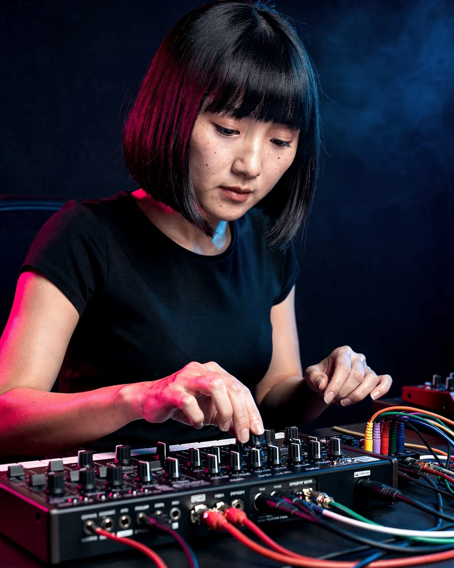 Music producer adjusting an analog synthesizer under blue and magenta lights